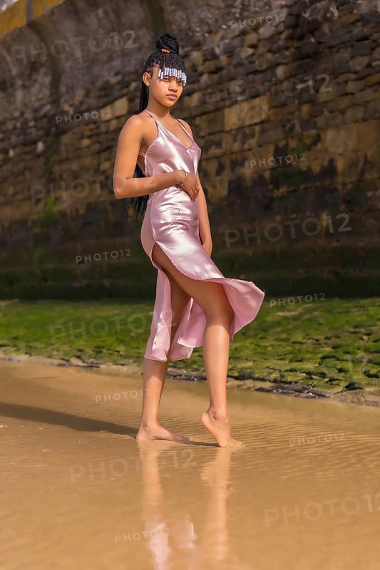 Dominican ethnic girl with braids with a beautiful pink dress. Fashionable posing enjoying summer on the beach