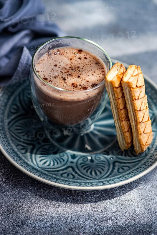 A delectable puff pastry filled with rich apricot jam alongside a steaming cup of freshly brewed cocoa, presented on a beautifully designed blue plate for a delightful treat