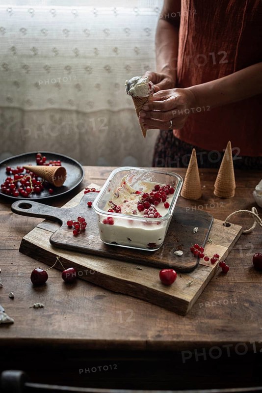 Cropped unrecognizable woman holding a cone filled with homemade ice cream, with additions of currants and gooseberries on a rustic table