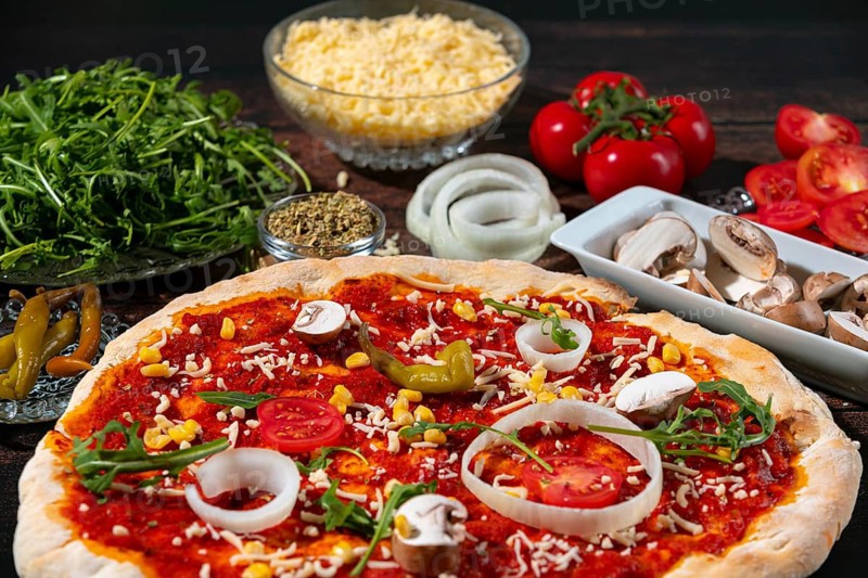 A vegetarian pizza surrounded by fresh ingredients such as tomatoes, onions and arugula