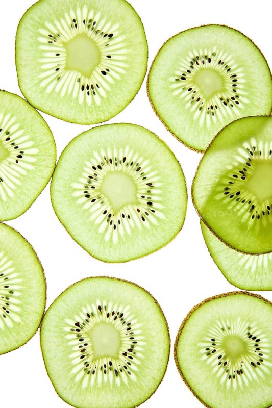 Close up of fresh kiwi slices arranged against a light background. The vibrant green fruit exhibits a detailed texture and seeds, highlighting its natural beauty and freshness