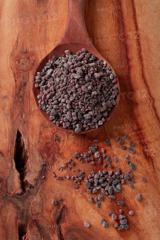 Crystals of black salt, on a wooden spoon, laid out on a wooden surface, top view