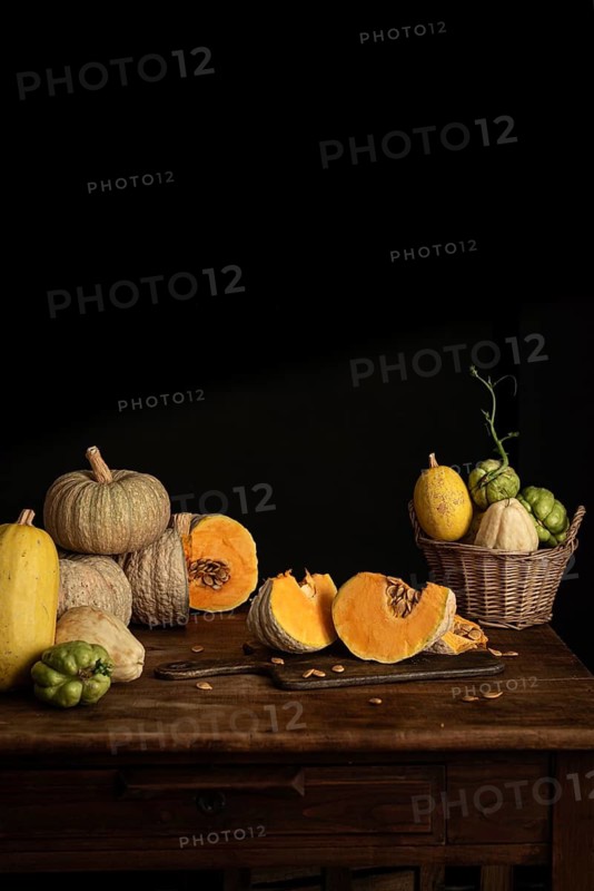 A variety of pumpkins and chayote with vibrant orange and green hues arranged on a rustic wooden table against a dark backdrop, evoking an autumnal harvest scene