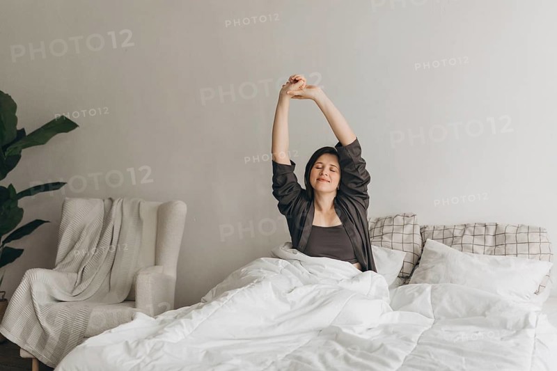 A woman stretches in bed, enjoying a morning routine promoting energy and wellness. The serene setting emphasizes balance and well-being, ideal for a healthy lifestyle theme