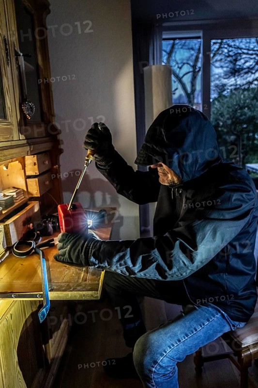 Symbolic image of a burglary, perpetrator has broken into a flat from the garden side and is looking for loot, breaks open a cash box, valuables, money