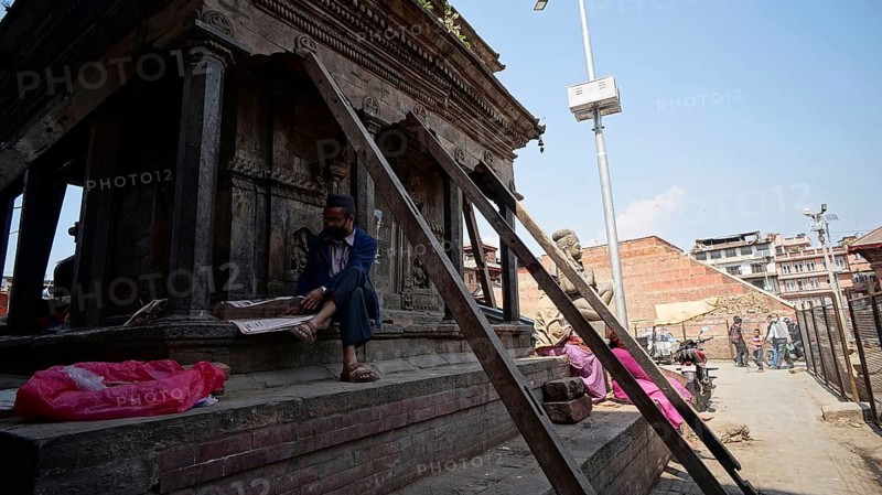 Man sits in front of a temple secured by support beams on Durbarsquare in Kathmandu and reads a newspaper shortly after the earthquake, Kathmandu, Nepal
