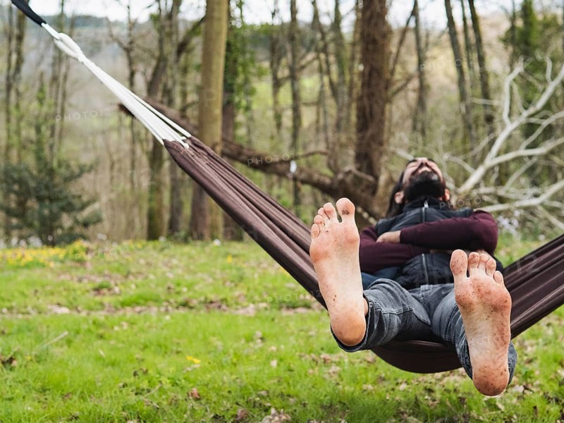 A man reclines comfortably in a hammock amidst a tranquil forest, enjoying the serene natural setting. Lush green trees and soft sunlight create a peaceful ambiance