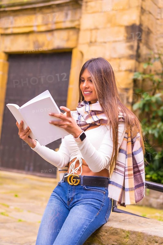 A young Latin woman with a white t-shirt, jeans and a scarf enjoying reading a book, in the old town of Pasaje San Juan, Gipuzkoa, Pais Vasco