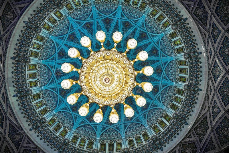 From below a captivating view of the ornately decorated dome and chandelier inside Sultan Qaboos Mosque in Muscat, Oman, showcasing intricate Islamic art