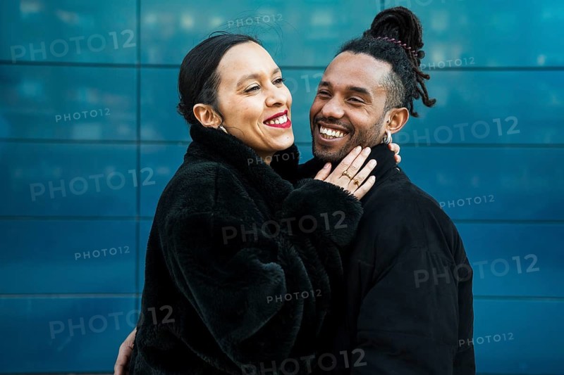 A multiethnic couple shares a joyful embrace, symbolizing unity and diversity. The modern backdrop enhances the image's contemporary feel, highlighting genuine happiness