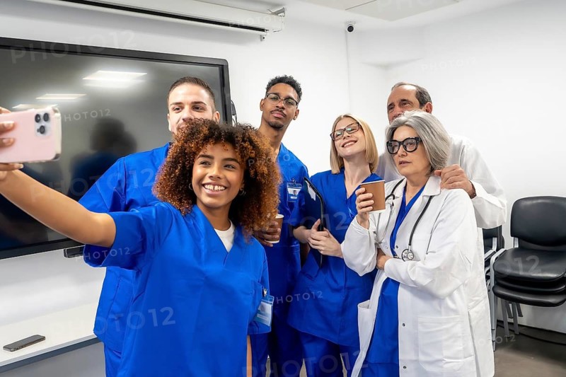 Group of smiling multi ethnic doctors, nurses, and medical personnel posing for a selfie using a cell phone, symbolizing joyful collaboration, modern communication, and staff unity