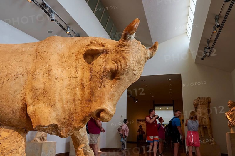 Large bull statue in a museum with visitors in the background, Olympia Archaeological Museum, Ancient Olympia, Peloponnese, Greece