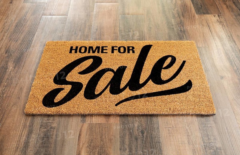 Home For Sale Welcome Mat On A Wood Floor Background