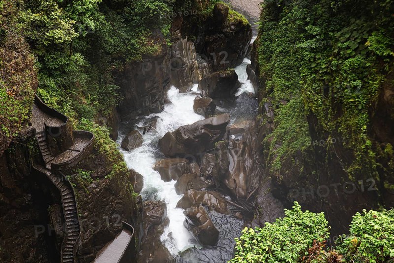 Spectacular view of a cascading waterfall surrounded by lush greenery near El Altar volcano, Ecuador. A winding rock staircase offers a stunning and adventurous path