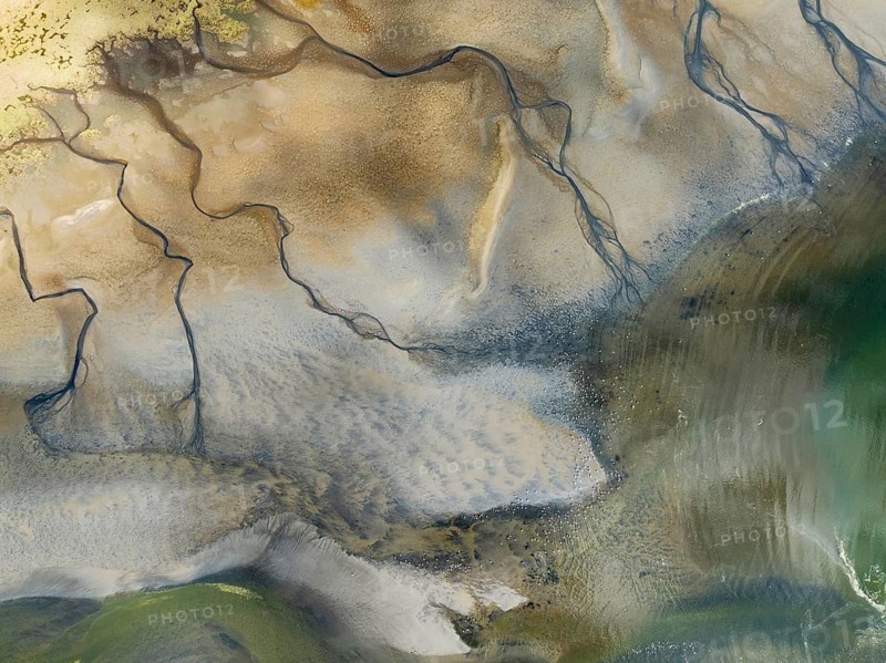 Streams and marshes at low tide in the coastal wetlands of the Walvis Bay lagoon. In the distance Greater Flamingos (Phoenicopterus ruber). Aerial view. Drone shot. Walvis Bay, Namibia