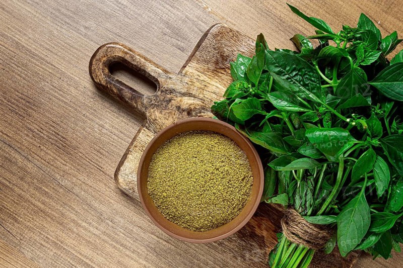 Ground green basil, in a ceramic bowl, with a bouquet of fresh green basil, on the table, top view, no people