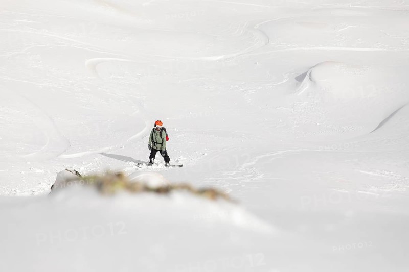 A snowboarder navigates through untouched powder in a remote mountain terrain. This exhilarating freeride captures the essence of extreme snow sports and winter adventure