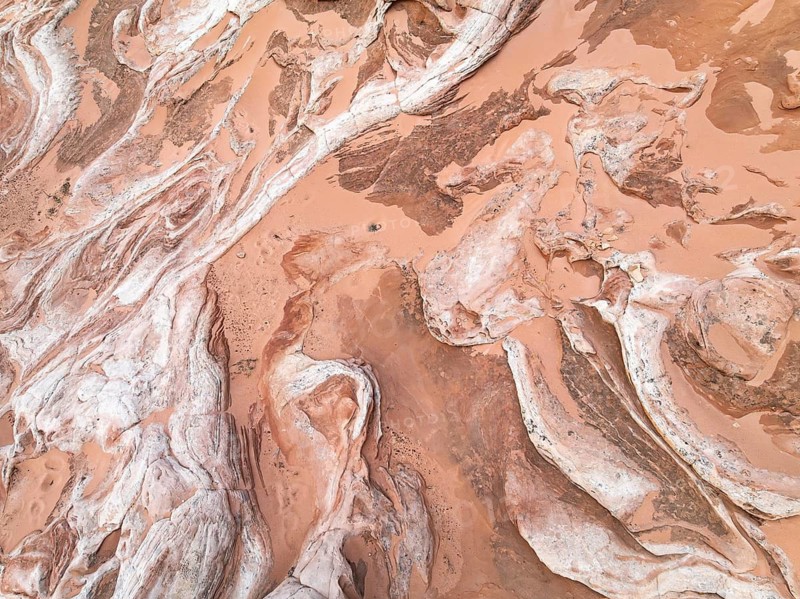 Aerial view of a red desert landscape, showcasing intricate textures and patterns formed by natural erosion. The image highlights the rich earthy tones and unique geological formations