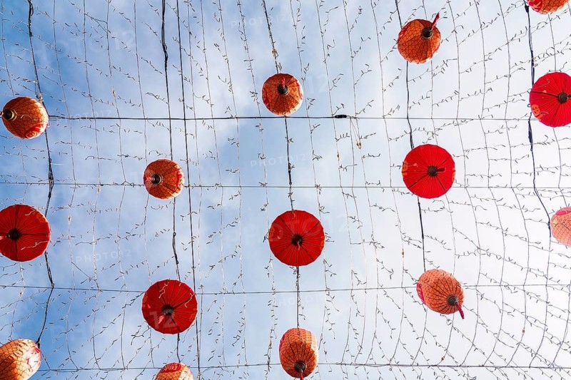Fromm below a cluster of traditional red Chinese lanterns suspended from cords against a clear blue sky, creating a vibrant pattern in the streets of Macau