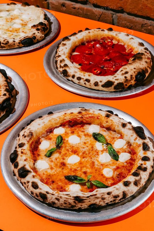 Wood-fired Margherita pizza with mozzarella, tomato sauce, basil, and oregano, paired with Pepperoni pizza featuring salami, mozzarella, tomato sauce, and chili pepper for a spicy kick