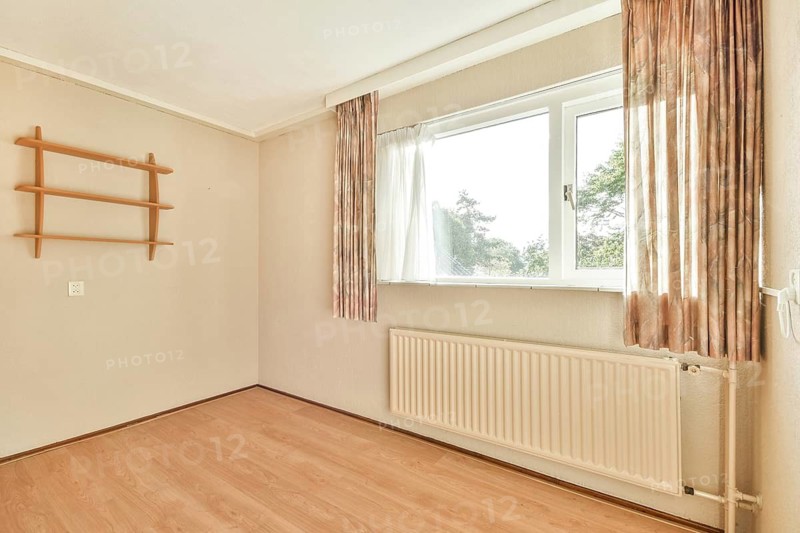 A spacious, bright room featuring large windows that allow ample natural light, complemented by light-colored walls and wooden flooring, creating a serene atmosphere