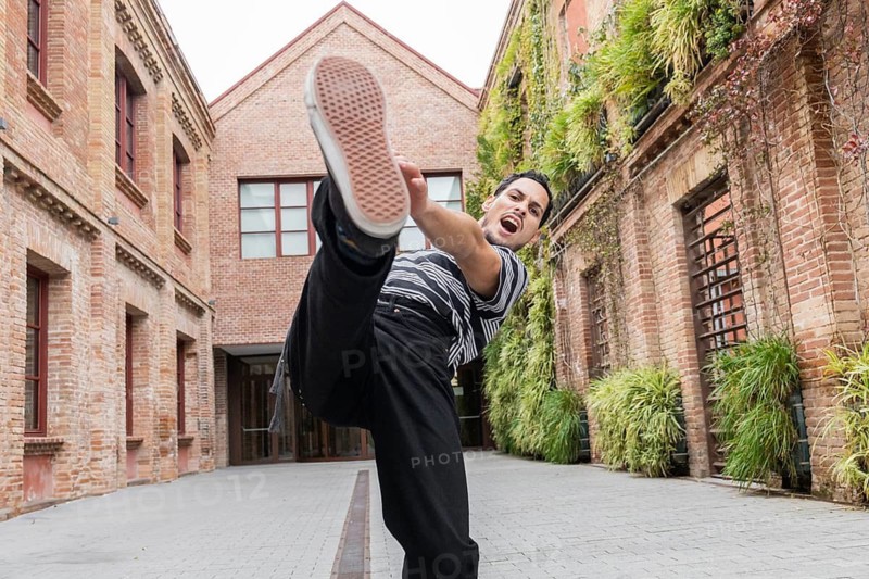 A dynamic Cuban dancer in mid-kick, radiates energy in a vibrant urban courtyard. Surrounded by brick walls and greenery, he embodies movement and passion