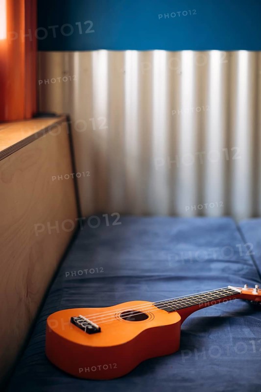A cozy Mexican interior features an acoustic ukulele resting on a plush blue sofa. The vibrant orange of the guitar contrasts the serene blue, evoking warmth and creativity