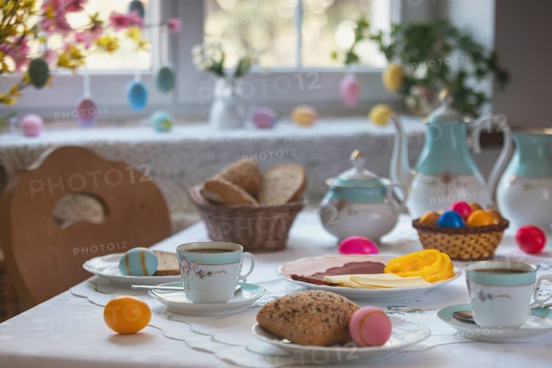 Breakfast table with Easter eggs, pastries and cold plate in front of decorated window