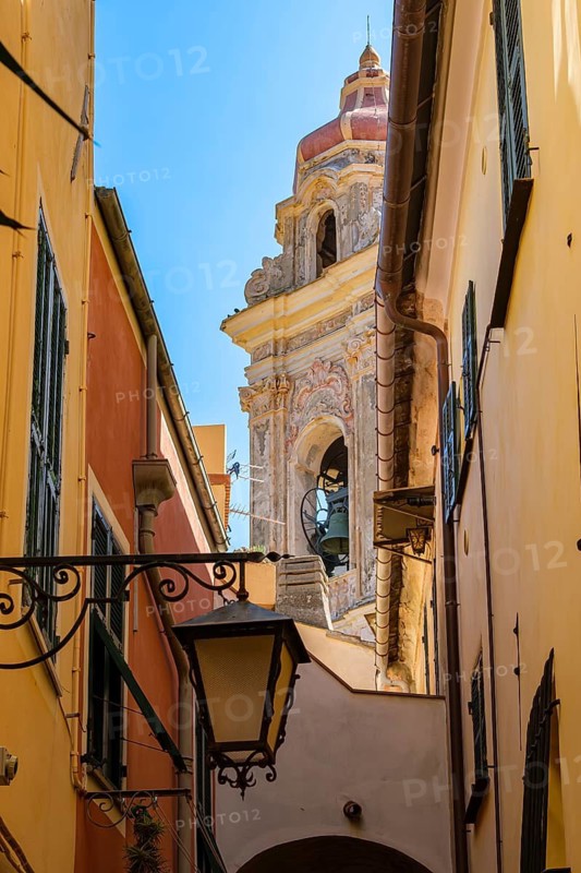 View through a picturesque narrow alley of the medieval old town to the tower of the baroque church of San Giovanni Battista, Cervo, Province of Imperia, Liguria, Italy