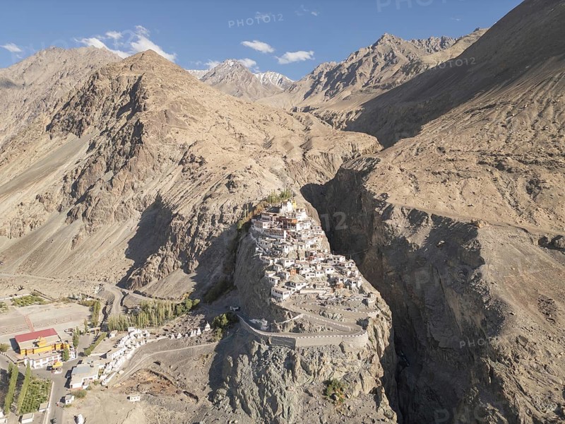 Aerial view of Diskit Gompa Monastery nestled in the rugged terrain of Nubra Valley, India, surrounded by dramatic mountains and clear blue sky, showcasing the area natural beauty