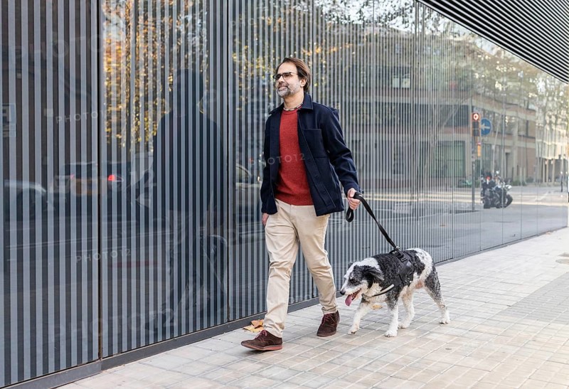 A middle-aged man enjoys a walk with his dog along a city street bordered by modern architecture. The image captures a daily lifestyle moment against a backdrop of urban refinement