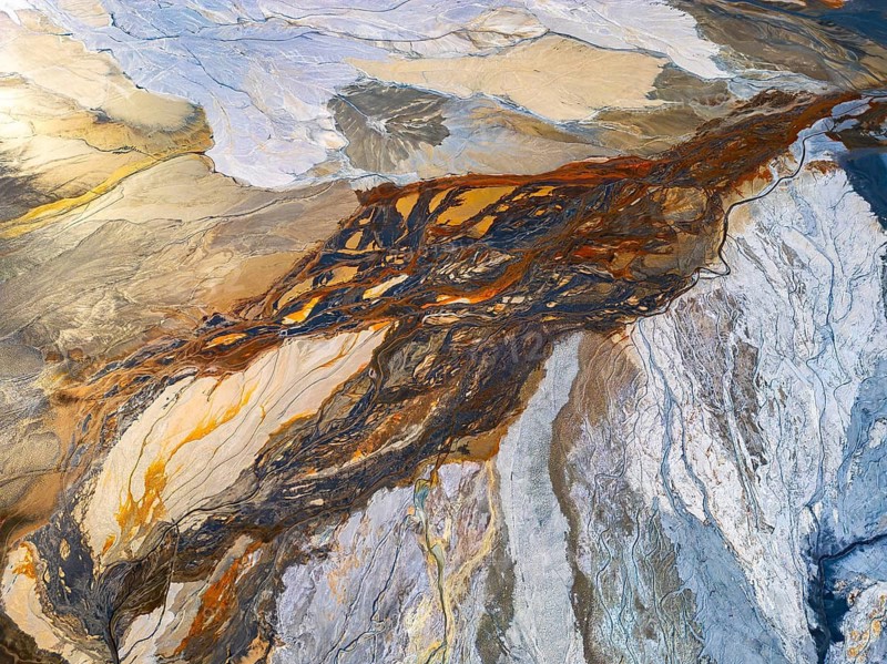From above, this aerial drone image captures the stunning interplay of abstract nature textures, featuring organic swirls and mixed hues that resemble an artist's palette