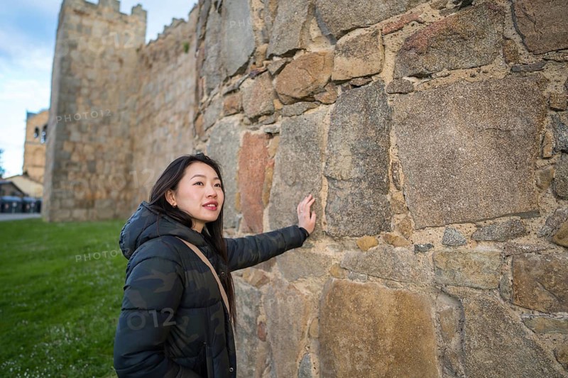 An Asian female tourist enjoys a memorable visit to Avila, Spain, exploring its impressive medieval walls and historic streets. She admires the town's rich cultural heritage