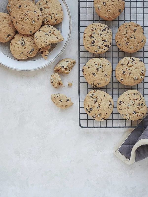 Freshly baked homemade chocolate chip cookies served in a plate and on a cooling rack with heat-resistant pad. Top view, copy space