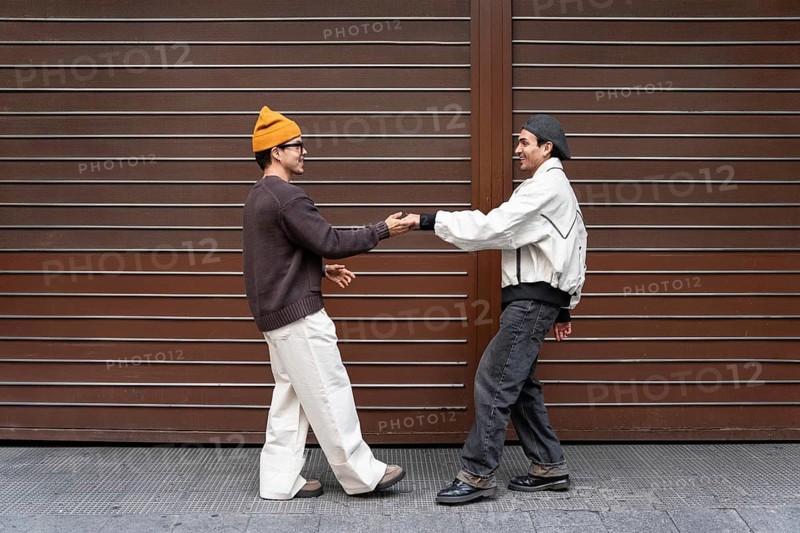 A Colombian couple enjoys a fun and carefree moment together outside, dancing against a modern brown backdrop