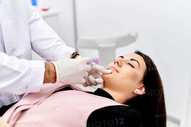 A beautician carefully injects hyaluronic acid into a patient's lips using a syringe. This procedure enhances the client's appearance, promoting fuller and more youthful lips