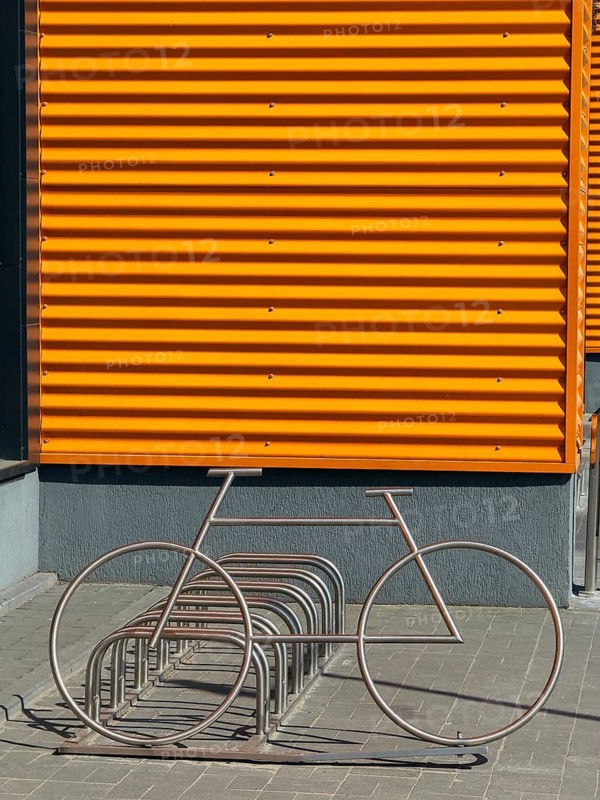 Modern industrial architecture featuring a bright orange metal wall and a creatively designed bicycle rack in the shape of a bike