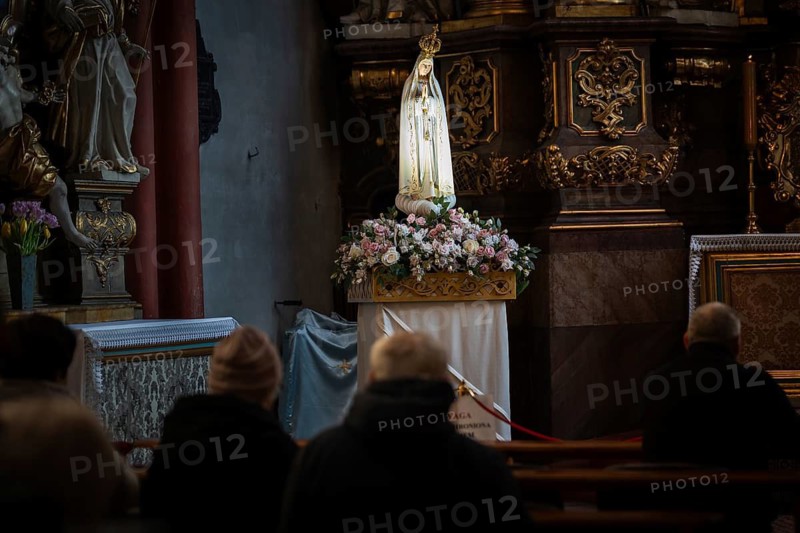 Devout people praying in a dim church before a flower-decorated statue of the Virgin Mary during a religious ceremony
