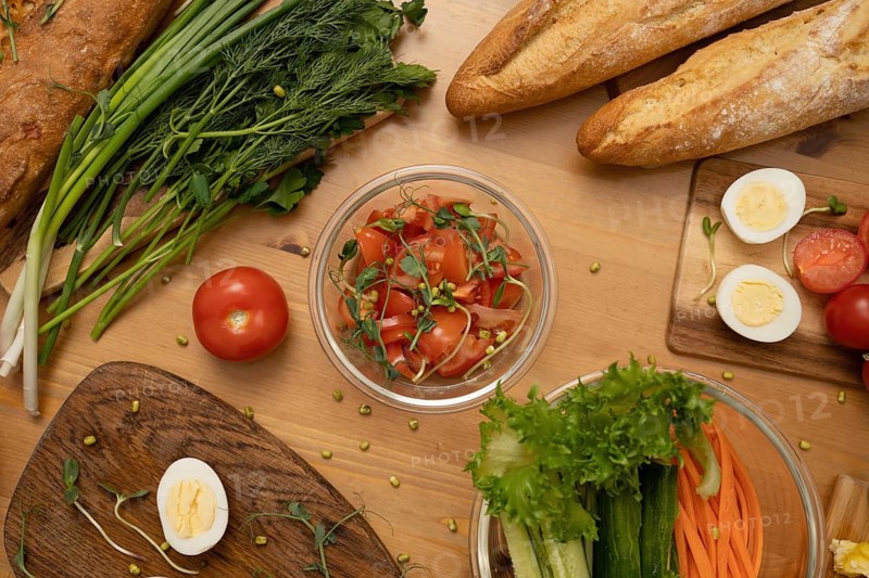 A vibrant tabletop spread featuring crusty baguettes, fresh vegetables, hard-boiled eggs, and a salad in a glass bowl, showcasing a healthy meal preparation setting