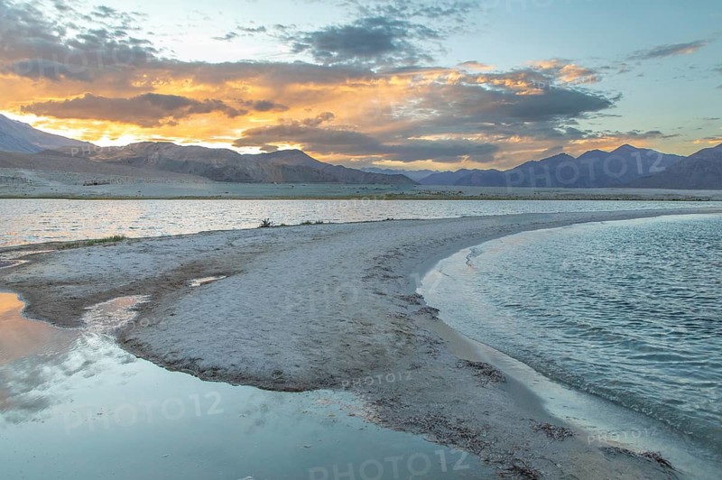 Breathtaking view of Pangong Tso lake in Ladakh at sunset. The tranquil waters reflect the vibrant hues of the sky, surrounded by the majestic Himalayan mountains