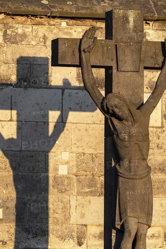 Stone cross with shadow cast at sunrise, cathedral cemetery near Cologne Cathedral, Cologne, North Rhine-Westphalia, Germany