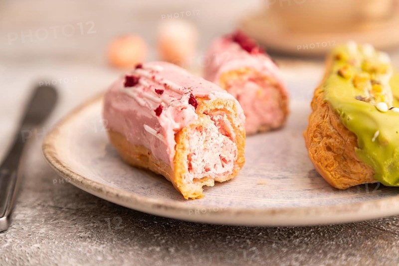 Glazed Eclairs on brown concrete background and green linen textile, cup of coffee, side view, close up, selective focus