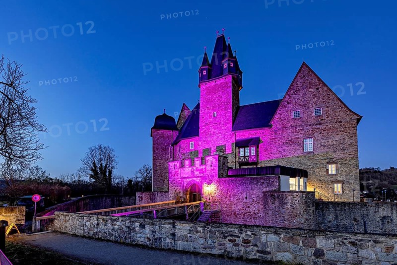 A castle at night, illuminated by pink light with dramatic-looking walls, Spangenberg Castle