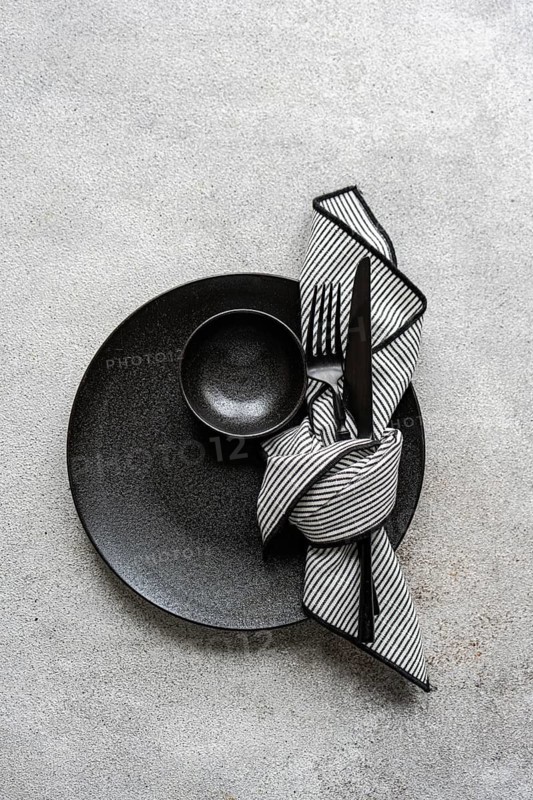 Elegant black and white table setting featuring a black plate, bowl, and cutlery with a striped napkin. Perfect for modern, minimalist dining themes