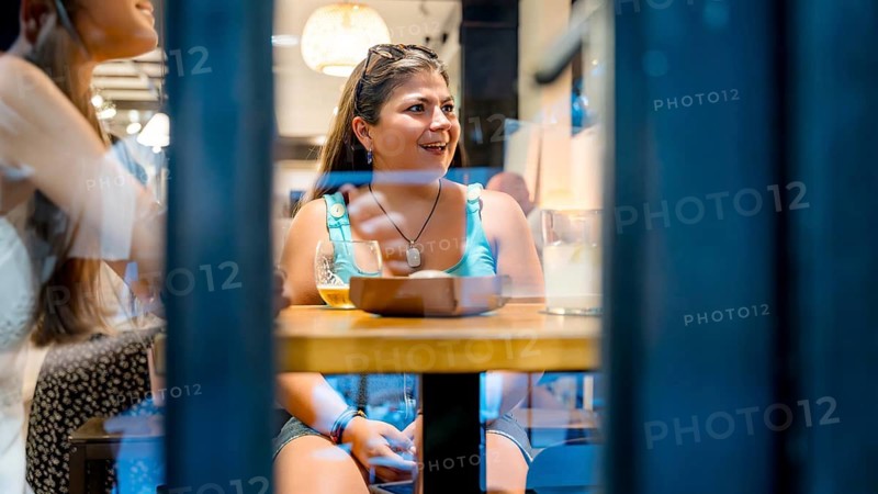 A woman enjoying dinner with friends in a cozy, warmly-lit restaurant. She is seated at a table with drinks and food, smiling and engaged in pleasant conversation