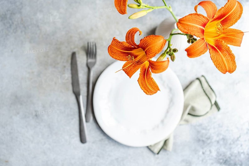 Top view of a vibrant orange tiger lily flower elegantly placed in a white vase on a minimalist dining table setting, creating a harmonious interior decor scene