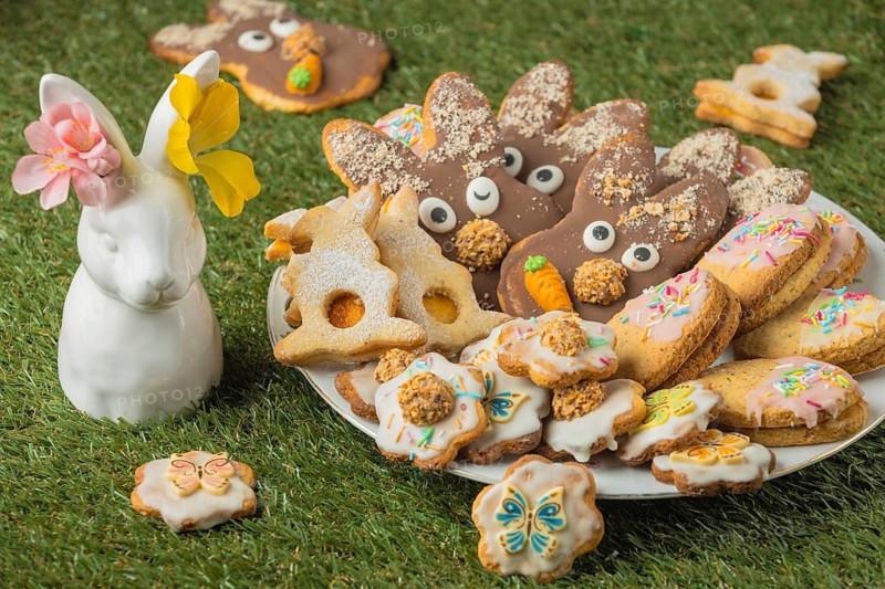 Different Easter cookies on a plate next to a porcelain hare with flowers in the grass