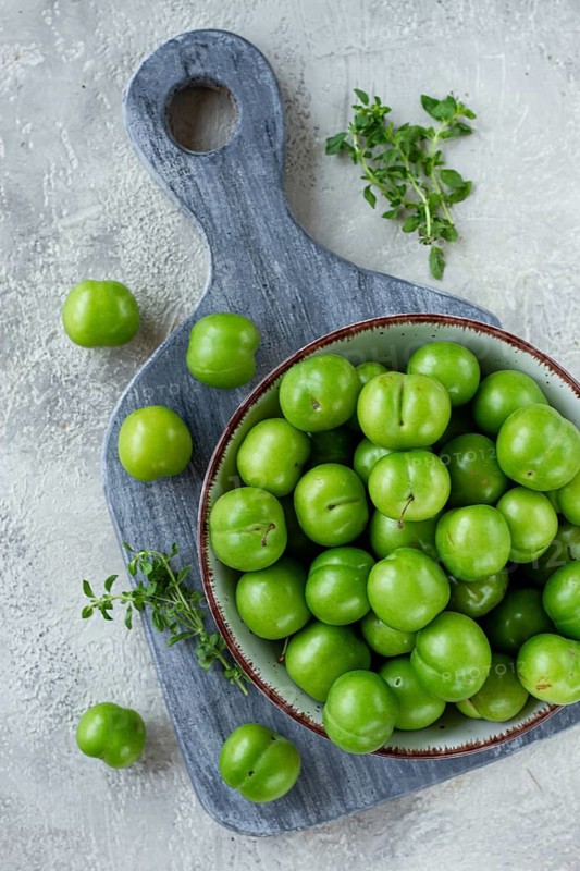 Tkemali, green cherry plum, in a bowl, on a gray table, top view, natural light, no people