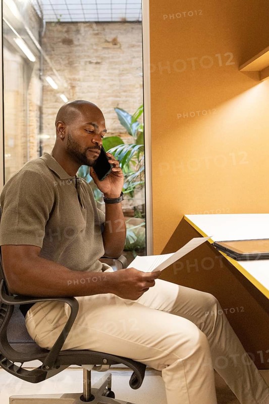 Professional working inside a modern coworking space in Barcelona. He's seated at a desk, engaged on the phone while reviewing documents, highlighting a productive atmosphere