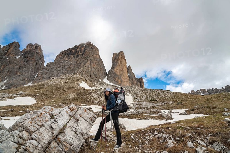A mother with a baby in a carrier enjoying a scenic hike in the majestic Tre Cime di Lavaredo, Dolomites. Rocky terrain, snow patches, and mountain peaks dominate the landscape